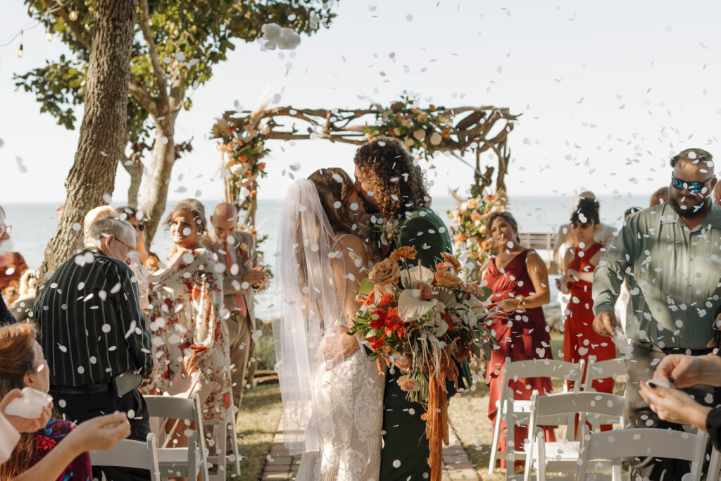 Bride and groom surrounded by friends during ceremony celebration with flower pedals