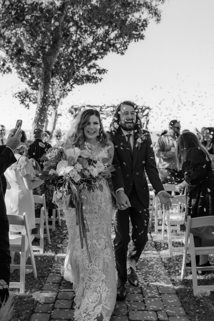bride and groom walk down aisle together after ceremony while guests throw flower pedals