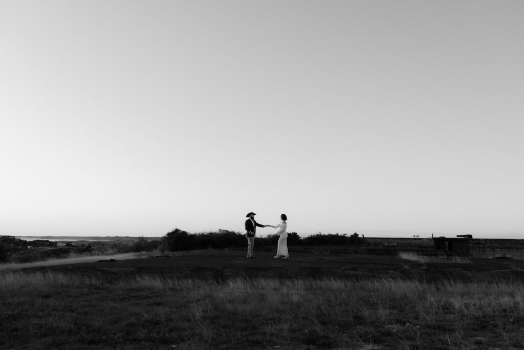 black and white photo of a first dance at sunset during Fort Pickens elopement, with bride holding her belly gently