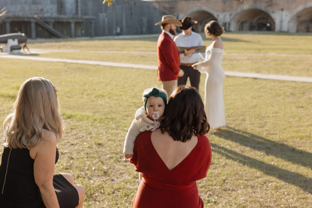 Fort Pickens elopement ceremony under a tree with benches, surrounded by family and sunlight