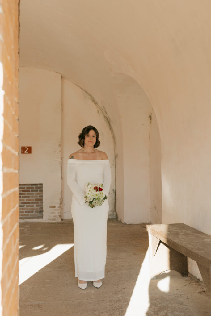 Bride standing quietly before her Fort Pickens elopement, holding flowers and taking a breath