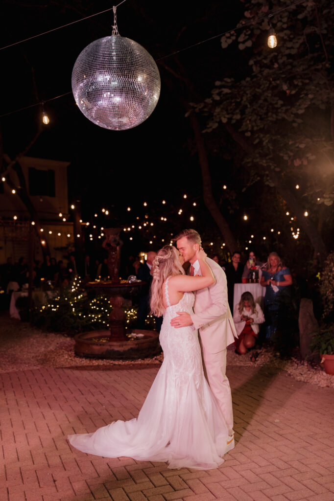 Couple dancing beneath disco ball and hanging garden lights at 30A wedding reception