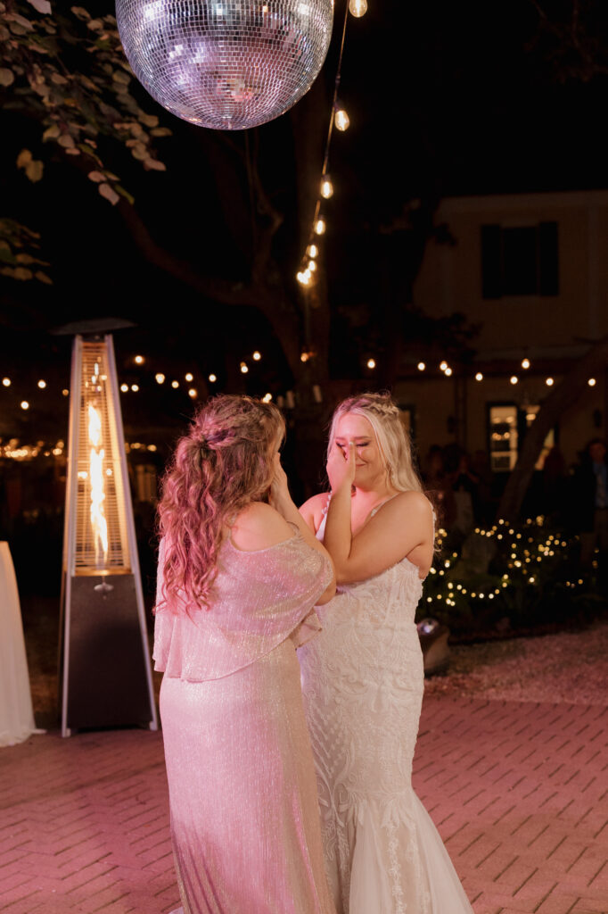 bride crying and dancing with mom beneath disco ball and hanging garden lights at 30A wedding reception
